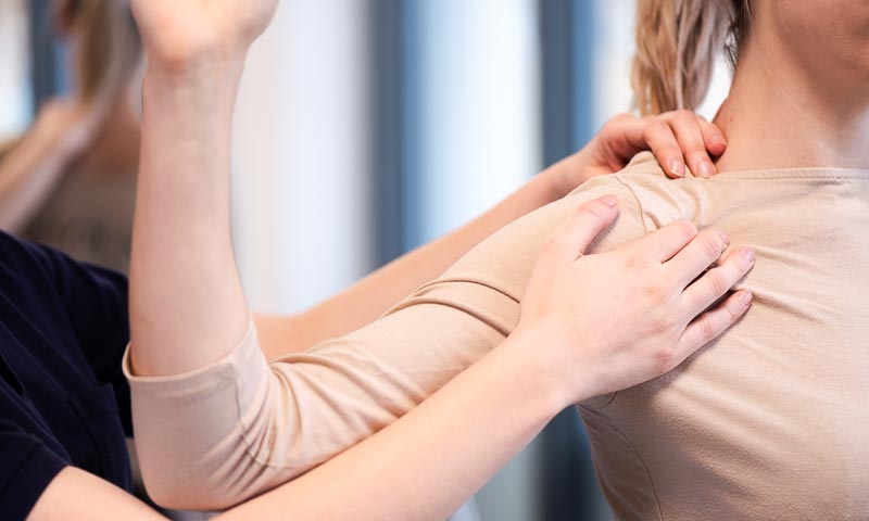 Physiotherapeutin behandelt Schulter einer Patientin